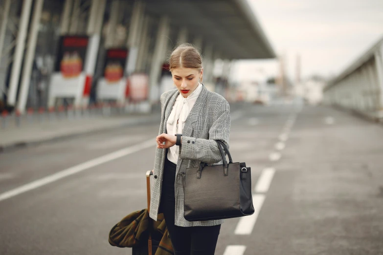 a woman standing on the side of a road looking at her cell phone, pexels contest winner, minimalism, holding a briefcase, wearing black grey suit, airport, cropped shirt with jacket