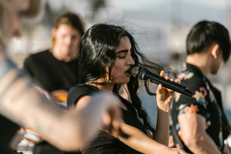 a woman singing into a microphone in front of a group of people, an album cover, by Niko Henrichon, pexels contest winner, on the coast, charli bowater, sydney park, closeup - view