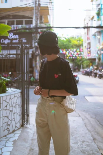 a man standing on a sidewalk looking at his cell phone, by Kun Can, unsplash, baggy clothing and hat, vietnamese woman, wearing black tshirt, offwhite