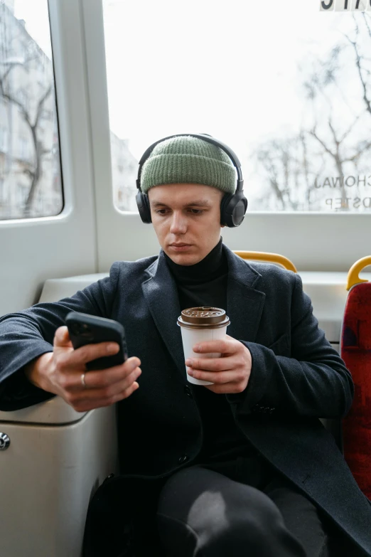 a man sitting on a bus looking at his cell phone, an album cover, trending on pexels, coffee cup, gaming headset, joe keery, swedish