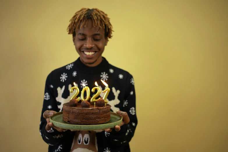 a person holding a cake with candles on it, an album cover, trending on pexels, he is wearing a brown sweater, black teenage boy, new years eve, 2 0 2 2 photo