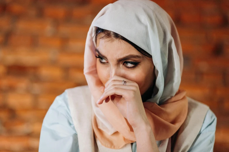 a woman in a hijab covers her face with her hands, trending on pexels, hurufiyya, handsome girl, staring hungrily, arabian nights inspired, white scarf