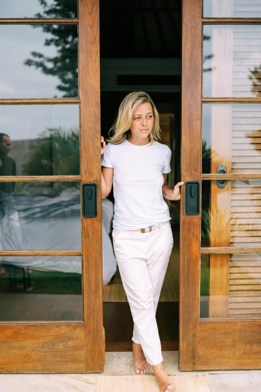 a woman standing in front of a wooden door, dressed in a white t shirt, sydney sweeney, white belt, hollister ranch