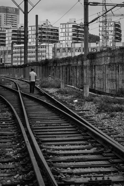 a black and white photo of a train track, by Joze Ciuha, man walking through city, yard, a very sad man, seen from a distance