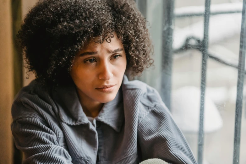 a woman with curly hair sitting in front of a window, a portrait, trending on pexels, sad man, ashteroth, curly bangs, clinically depressed