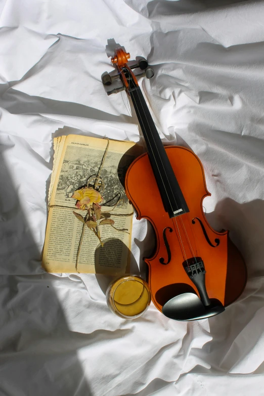 a violin sitting on top of a bed next to a book, yellow, honey, set photograph, high angle shot