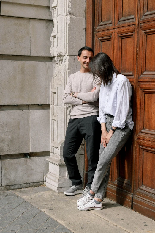 a man and a woman leaning against a wooden door, a picture, by Nina Hamnett, wearing white sneakers, in london, profile image, wearing pants