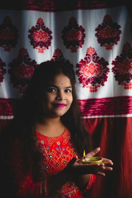 a woman holding a lit oil lamp in her hand, an album cover, pexels contest winner, wearing a kurta, portrait mode photo, student, crimson themed