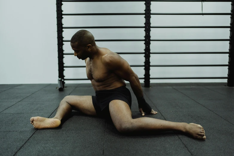 a man sitting on the ground in a gym, a photo, by Jessie Alexandra Dick, doing splits and stretching, man is with black skin, profile image, sydney hanson