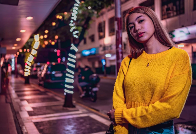 a woman standing on a city street at night, a portrait, pexels contest winner, sweater, yellow, set on singaporean aesthetic, nightlife