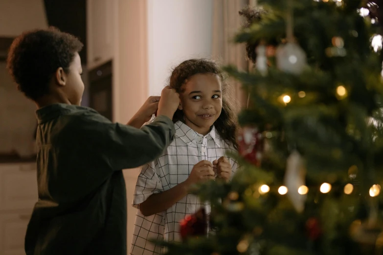 a couple of kids standing next to a christmas tree, pexels contest winner, happening, hair, profile image, brown, decoration around the room