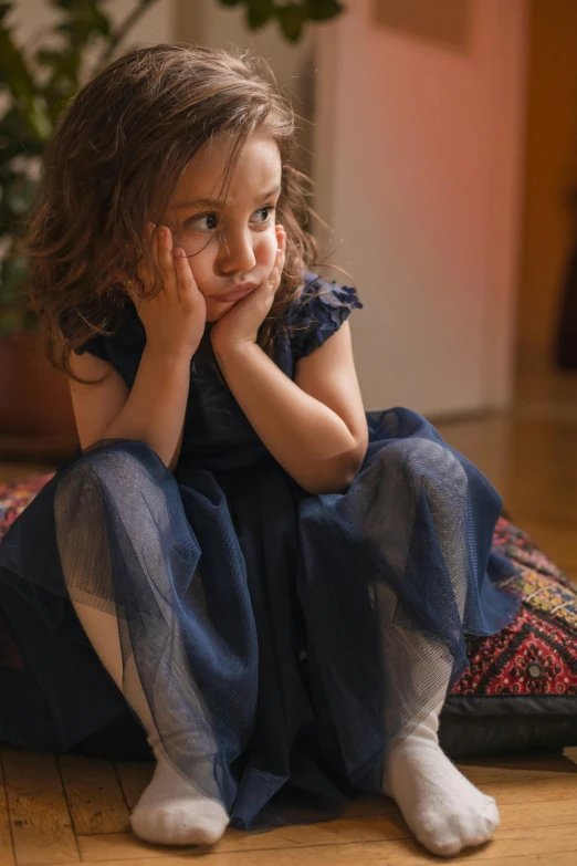 a little girl sitting on a pillow on the floor, by Jakob Gauermann, pexels, renaissance, concerned expression, navy, dress in voile, evening mood