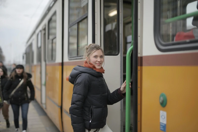 a woman is standing at the door of a bus, by Emma Andijewska, happening, trams ) ) ), warm friendly expression, orange line, brown