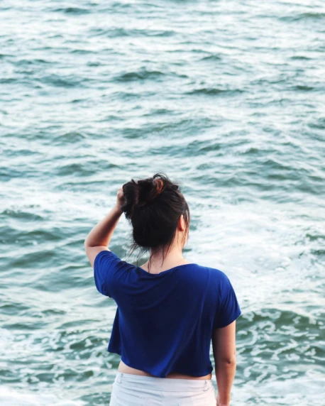 a woman standing on top of a beach next to the ocean, navy hair, lgbtq, girl with messy bun hairstyle, trending photo