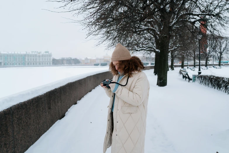 a woman standing in the snow using a cell phone, inspired by Louisa Matthíasdóttir, pexels contest winner, visual art, brown tuffle coat, saint petersburg, white coat, scenery