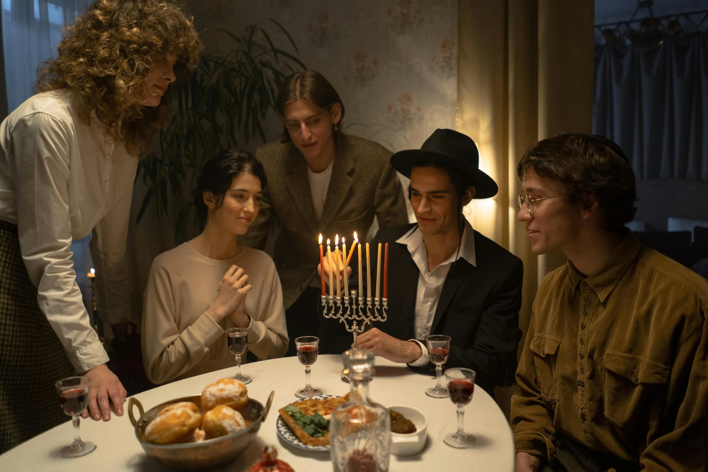 a group of people sitting around a table with a menorah, natalia dyer, hammershøi, festive atmosphere, digital image