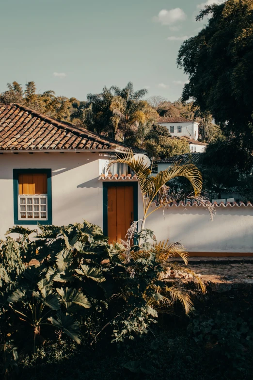 a white house sitting on top of a lush green field, by Lucas Vorsterman, pexels contest winner, modernism, colonial era street, warm light, tropical setting, little cottage