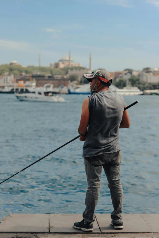a man standing next to a body of water holding a fishing rod, by Cafer Bater, pexels contest winner, hurufiyya, fallout style istanbul, sittin, ox, low quality photo