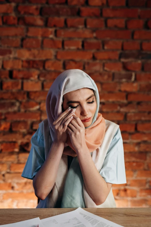 a woman sitting at a table with her hands on her face, hurufiyya, hijab, heartbroken, 2019 trending photo, sweating intensely