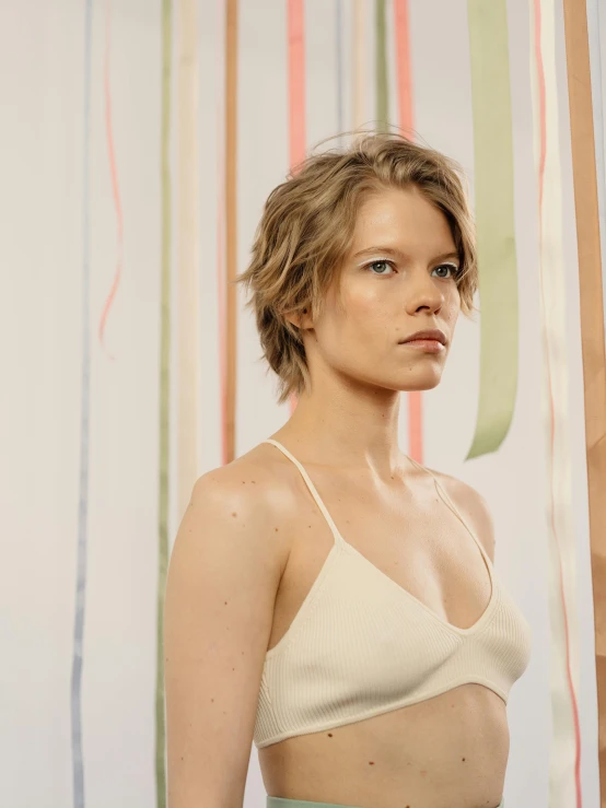 a woman standing in front of a striped wall, inspired by Vanessa Beecroft, trending on unsplash, bralette, milla jovovich, wearing wheat yellow gauze, bleached blonde short hair