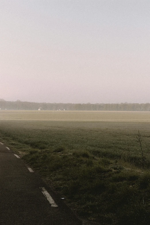 a person riding a bike down a road on a foggy day, by Daarken, color field, on a soccer field, cinematic shot ar 9:16 -n 6 -g, panorama distant view, grassy field