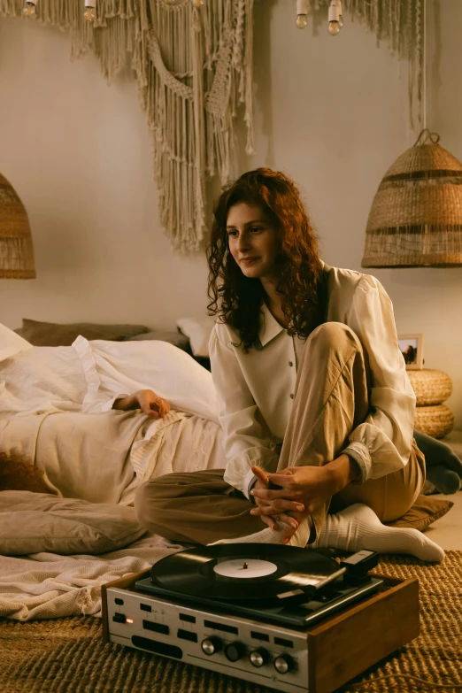 a woman sitting on a bed next to a record player, wearing a linen shirt, evening ambience, beige, wearing nanotech honeycomb robe