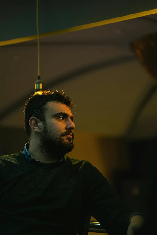 a man that is sitting down with a remote in his hand, an album cover, by Youssef Howayek, pexels contest winner, hurufiyya, dark cables hanging from ceiling, looking from side, at a bar, ((portrait))