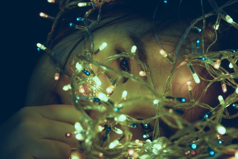 a close up of a person holding a string of lights, a picture, inspired by Elsa Bleda, trending on pexels, intricate heterochromatic sad, teenager girl, christmas night, with instagram filters