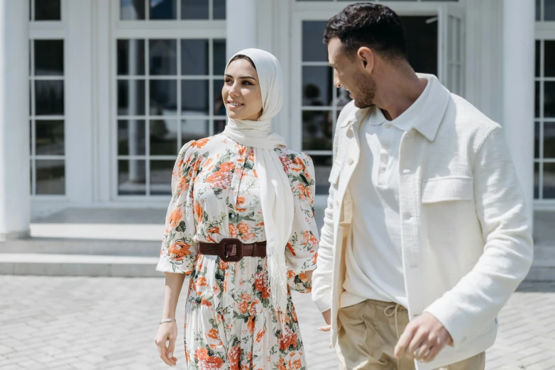 a man and a woman walking in front of a building, trending on pexels, hurufiyya, floral clothes, young middle eastern woman, at home, wearing white clothes