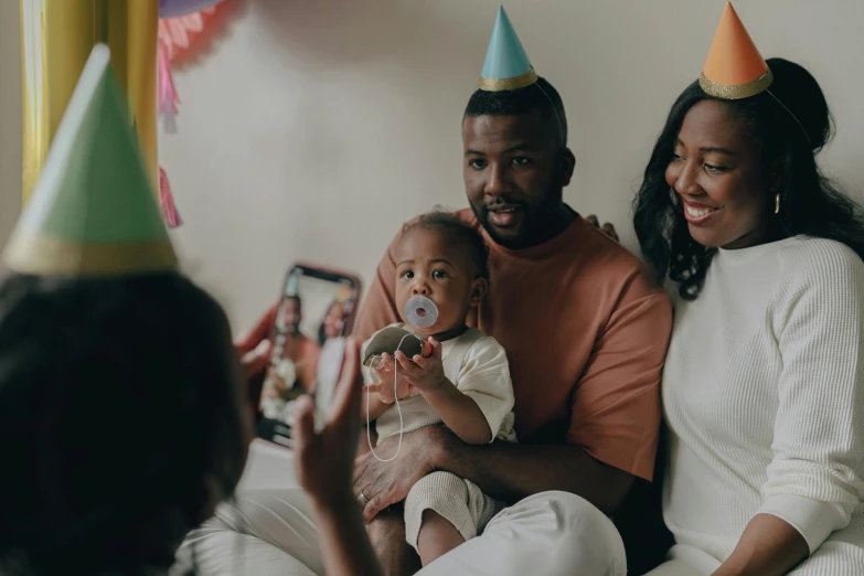 a man and woman sitting on a couch with a baby, pexels contest winner, happening, party hats, photo of a black woman, hold up smartphone, happy birthday