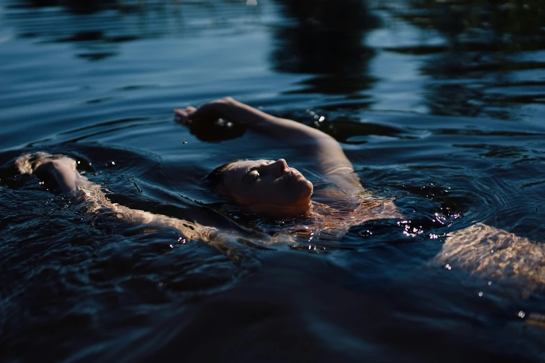 a person swimming in a body of water, inspired by Elsa Bleda, unsplash, process art, dark blue water, late summer evening, sunbathed skin, ophelia