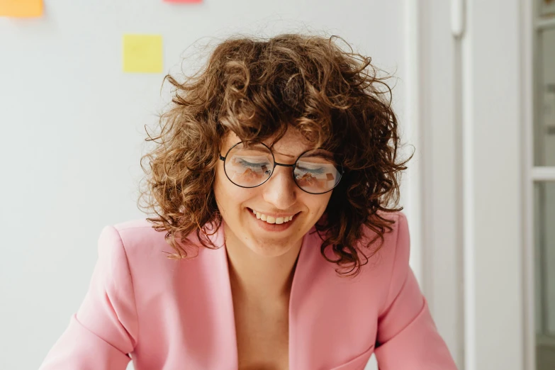 a woman sitting at a table in front of a laptop computer, by Nina Hamnett, pexels contest winner, curly haired, pink glasses, ai researcher, wearing a light - pink suit