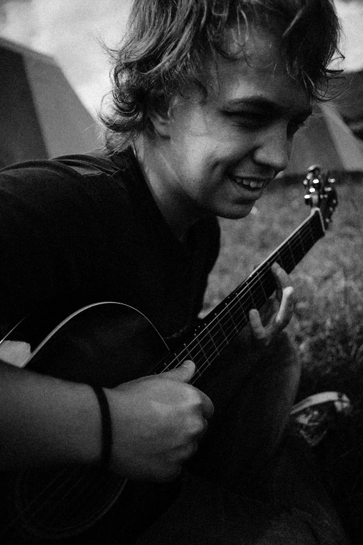 a black and white photo of a man playing a guitar, by Jacob Toorenvliet, smiling sweetly, harry styles, he is at camp, smol