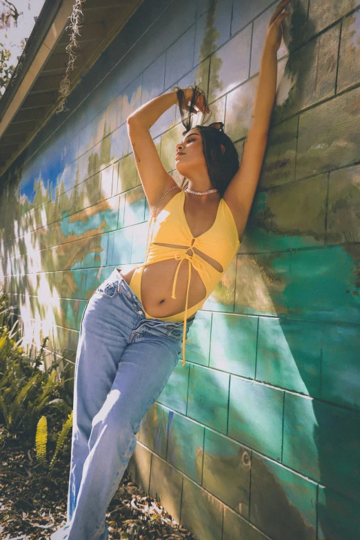 a woman leaning against a wall with her arms in the air, an album cover, by Robbie Trevino, trending on pexels, wearing yellow croptop, full body:: sunny weather::, 🐿🍸🍋