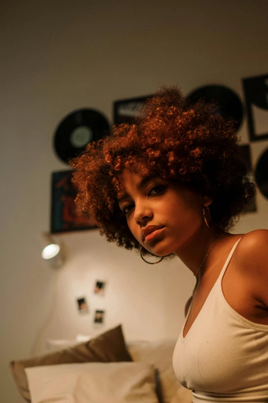a woman in a white tank top sitting on a bed, an album cover, inspired by Nan Goldin, trending on pexels, afro hair, vibrant lights, complementary lighting, in her room