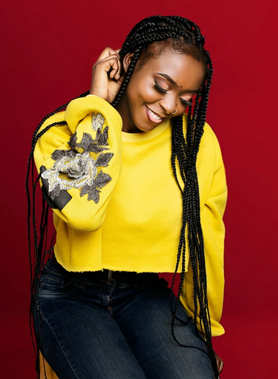 a woman sitting on top of a wooden chair, inspired by Chinwe Chukwuogo-Roy, trending on pexels, wearing yellow croptop, wearing a hoodie and flowers, long black braids, promotional image