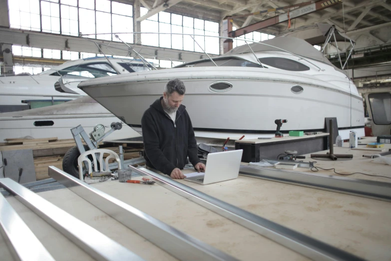 a man working on a laptop in a boat repair shop, unsplash, precisionism, galvalume metal roofing, avatar image, full body image