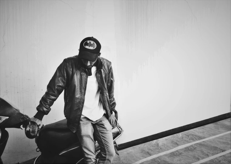 a black and white photo of a man standing next to a motorcycle, unsplash, graffiti, : kendrick lamar, with hat, leaving a room, brown leather jacket