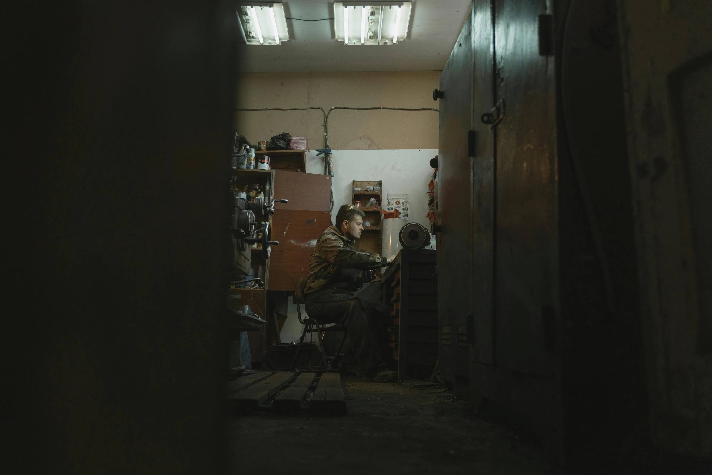 a man sitting in a chair in a dark room, inspired by Elsa Bleda, pexels contest winner, inside an old weapon shop, ismail inceoglu and ruan jia, cinestill 8 0 0 tungsten 3 5 mm, medium format. soft light