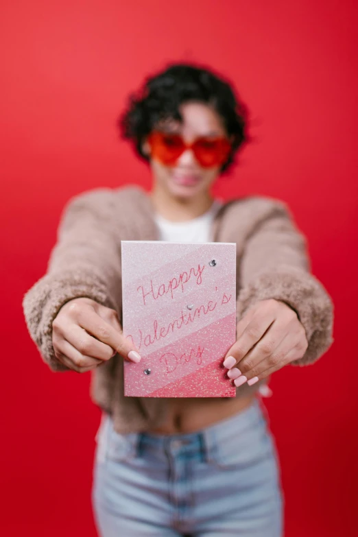 a woman holding a card that says happy valentine's day, an album cover, pexels, happening, wearing shades, product introduction photo, glitter accents on figure, andrew gonzalez