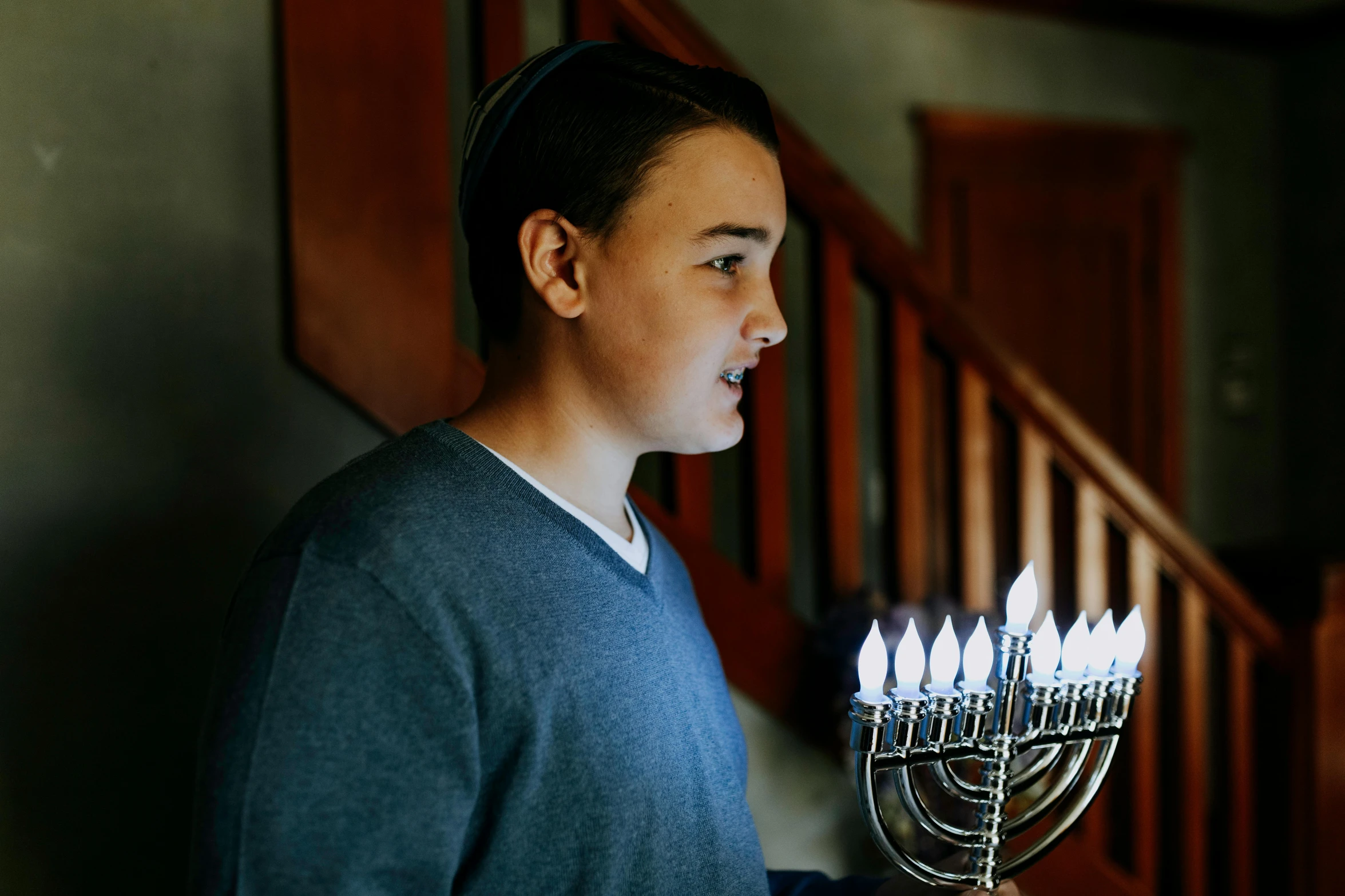 a man holding a menorah with lit candles on it, a colorized photo, by Carey Morris, pexels, teen boy, wearing festive clothing, avatar image, candid shot