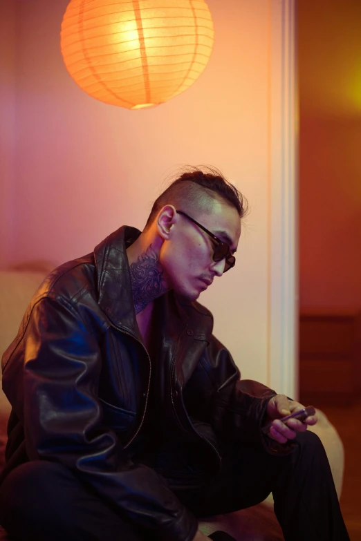 a man in a leather jacket sitting on a couch, inspired by Zhu Da, trending on pexels, visual art, shaved sides, bisexual lighting, tattooed, phone photo