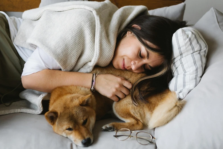 a woman laying on top of a bed next to a dog, by Julia Pishtar, trending on pexels, renaissance, cuddling her gremlings, shibu inu, recovering from pain, relaxing on the couch