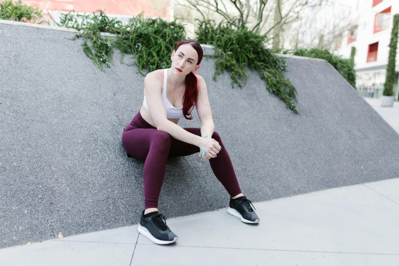 a woman sitting on top of a cement wall, pexels contest winner, train with maroon, wearing fitness gear, extremely pale white skin, on a sidewalk of vancouver