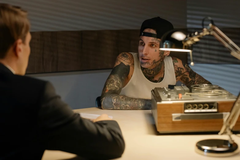 a man sitting at a desk in front of a microphone, a tattoo, marshal mathers, calmly conversing 8k, commercial photo, radio