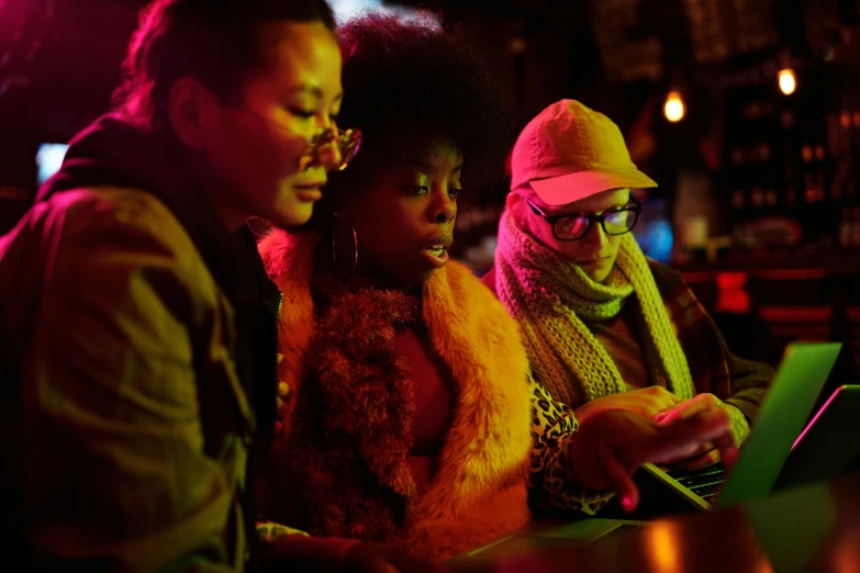 a group of people sitting at a bar looking at a laptop, pexels, afrofuturism, three women, warm coloured, [ theatrical ], night outside