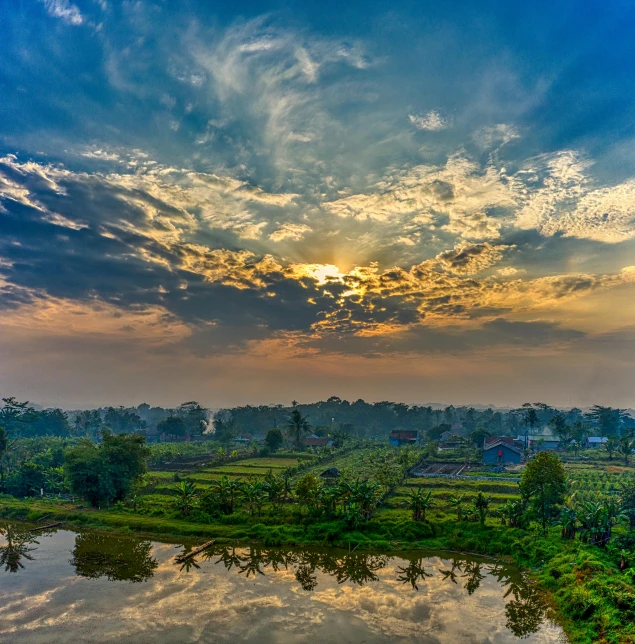 a river running through a lush green field under a cloudy sky, by Basuki Abdullah, pexels contest winner, sunset panorama, batik, kerala village, orange and blue sky