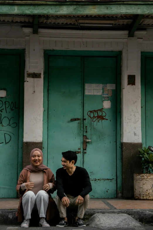 a man and a woman sitting in front of a building, pexels contest winner, south jakarta, green alleys, lesbians, background image