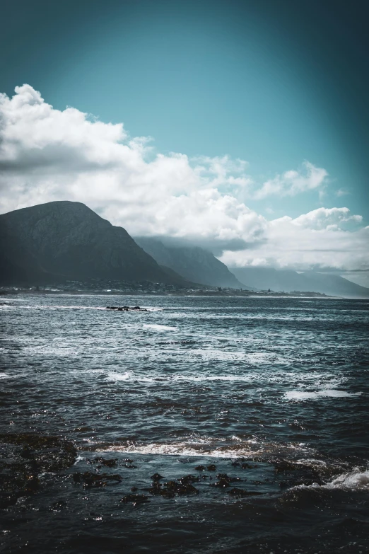 a body of water with a mountain in the background, by Jacob Toorenvliet, trending on unsplash, baroque, rough seas in background, cape, scattered clouds, high quality photo