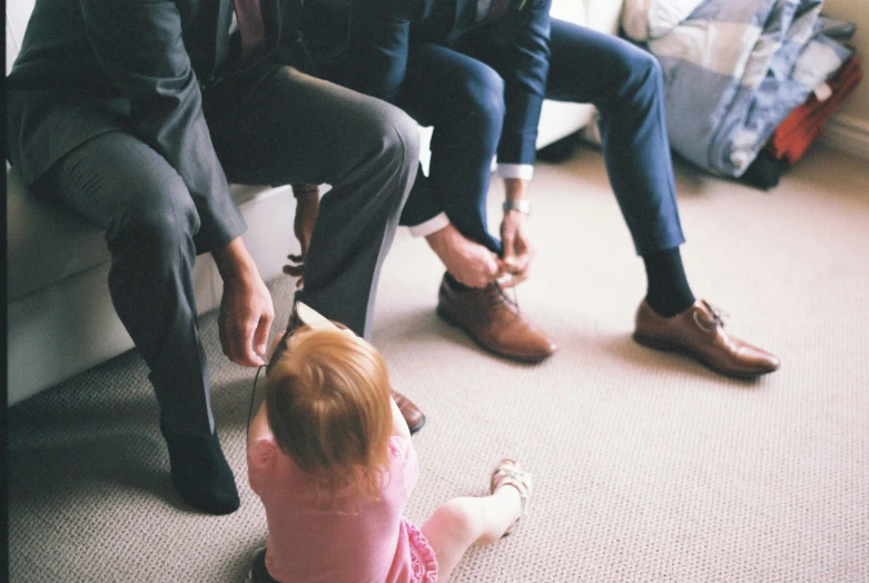 a little girl sitting on the floor next to a man, by Alice Mason, unsplash, groom, in a row, business men, pink shoes